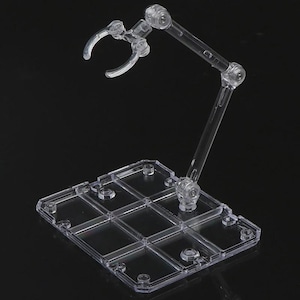 May include: A transparent plastic action figure stand with a rectangular base and an adjustable arm. The stand has a claw-like grip to hold the figure and multiple joints for posing. The stand is designed to provide support and display action figures.