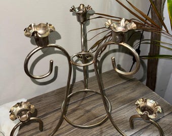 Puede incluir: Un candelabro de metal plateado con cuatro candeleros. Los soportes tienen un diseño en forma de flor y están unidos a brazos curvos. El candelabro tiene un tallo central y una base circular, ideal para una mesa.