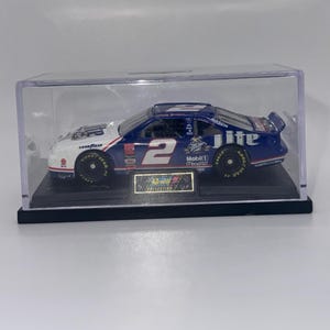 May include: A blue, white, and red diecast race car model in a clear display case. The car features the number 2, sponsor logos, and the words "Miller Lite." The model is on a black base with a gold plaque.