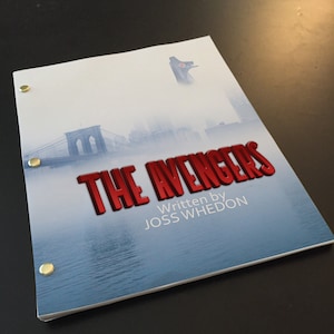 Può includere: Una copertina di sceneggiatura bianca con un titolo rosso che recita "THE AVENGERS" e il testo "Written by JOSS WHEDON". La copertina presenta un'immagine sfocata del ponte di Brooklyn e uno skyline sullo sfondo.