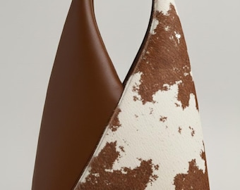 May include: A brown and white cowhide tote bag with a brown leather side and a woven handle. The bag has a unique triangular shape.