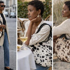 May include: A large, round handbag with a cowhide pattern in shades of brown, black, and white. The bag has a black leather handle and trim. The bag is being carried by a person in a casual outfit.