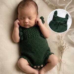 May include: A dark green crochet baby romper featuring ruffled shoulder straps, a textured bodice, and three small wooden buttons at the bottom. The text Baby Romper is visible in the upper right corner with an arrow pointing to the garment.