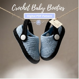 May include: A pair of light blue and black crochet baby booties hanging from a string. The booties feature a black strap with a white circular button on each side. Text reads Crochet Baby Booties and Digital PDF Pattern with a FIO A FIO tag.