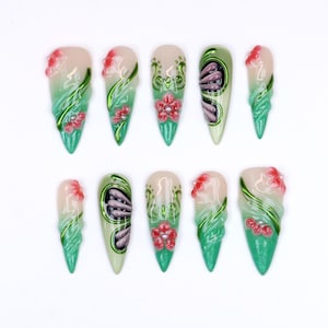 May include: Set of ten long, pointed artificial nails. Each nail features a gradient design of light pink to green, with red floral accents and green metallic swirls. Some nails have a seashell design.