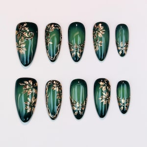 May include: A set of ten emerald green press-on nails with gold floral designs. The oval-shaped nails have a glossy finish. The gold floral accents are applied in various patterns, adding a touch of elegance to the design.