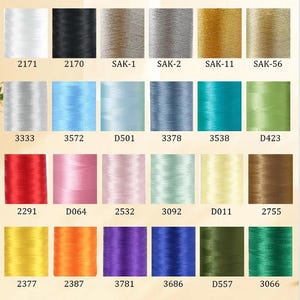 K&ouml;nnte beinhalten: Eine Farbkarte mit Stickgarnspulen in verschiedenen Farben, darunter Wei&szlig;, Schwarz, Silber, Gold, Blau, Gr&uuml;n, Rot, Rosa und Gelb. Jede Spule ist mit einer eindeutigen Nummer oder einem Code versehen.
