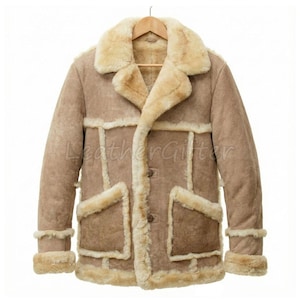 May include: A tan shearling coat with a cream-colored shearling lining and trim. The coat has a wide collar, two front pockets, and button closures. The sleeves have shearling cuffs. The text "LeatherGifter" is visible on the coat.