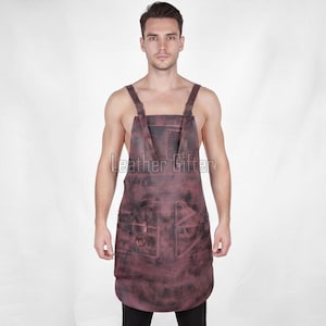 Könnte beinhalten: Eine dunkel rotbraune Lederschürze mit marmorierter Oberfläche, verstellbaren Schultergurten mit Metallschnallen, einer Brusttasche, zwei großen unteren Taschen und einem Metall-D-Ring. Der Text Leather Gifter ist auf der Brust aufgedruckt.
