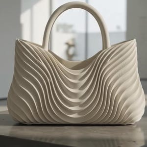 Könnte beinhalten: Eine cremefarbene Handtasche mit einer ausgeprägten dreidimensionalen, wellenförmigen Textur auf der gesamten Außenfläche. Die Tasche hat ein breites, offenes Design und einen einzelnen, stabilen, bogenförmigen Griff an der Oberseite.