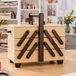 Peut inclure: Une boîte à couture rectangulaire avec une finition beige clair et des accents en bois brun foncé. La boîte dispose d'un mécanisme de pliage en accordéon à plusieurs niveaux avec une poignée centrale et quatre petits pieds.