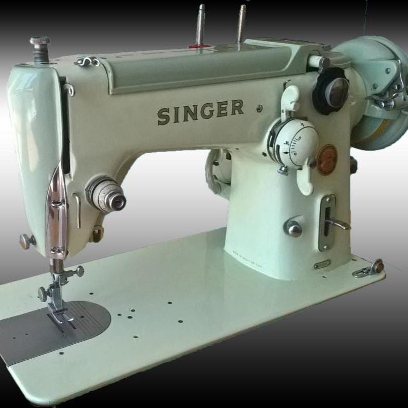 Könnte beinhalten: Eine Vintage Singer Nähmaschine in hellgrüner Farbe. Auf der Maschine steht das Wort "SINGER". Sie verfügt über verschiedene Zifferblätter, Hebel und eine Nadel mit einer flachen Basis zur Stoffplatzierung. Die Maschine steht vor einem dunklen Hintergrund. SINGER 201 306 316 319 215r