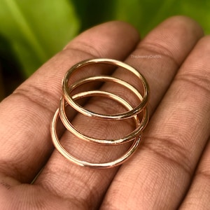May include: A set of three thin, polished rose gold-tone metal rings stacked together. Each ring features a smooth, rounded band with a reflective surface. The text TheJewelryCraftIN is visible in small, faint lettering near the top of the rings.