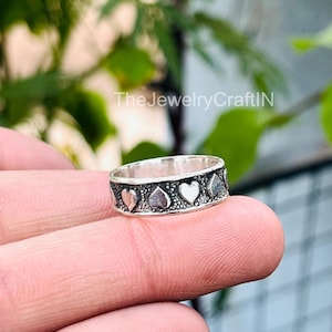 May include: A silver ring with a repeating heart pattern. The ring features alternating solid and dotted hearts around the band. The text "TheJewelryCraftIN" is visible in the background.