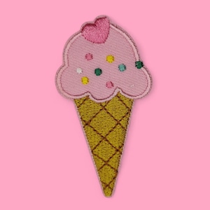 Könnte beinhalten: Gestickter Aufnäher eines rosa Eiswaffel mit einem Herz oben und bunten Streuseln. Der Kegel ist gelb mit einem Kreuzmuster. Der Hintergrund ist einfarbig rosa.