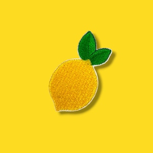 May include: Embroidered lemon patch with a bright yellow body and two green leaves. The patch has a white border and is set against a solid yellow background. Ideal for adding a touch of citrus to clothing or accessories.