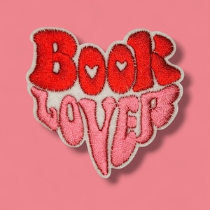 Könnte beinhalten: Gestickter Aufnäher in Herzform mit den Worten "Book Lover" in Rot und Rosa. Der Aufnäher hat einen weißen Rand und eine flauschige Textur, ideal zum Aufnähen auf Kleidung oder Accessoires.