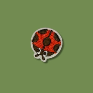 Könnte beinhalten: Gestickter Marienkäfer-Aufnäher mit rotem Körper, schwarzen Punkten und weißem Rand. Der Marienkäfer hat schwarze Augen und Fühler. Geeignet für Kleidung, Taschen oder andere Stoffartikel.