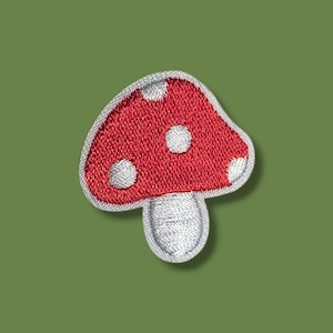 Puede incluir: Un parche bordado en rojo y blanco con forma de seta. El sombrero de la seta es rojo con puntos circulares blancos y el tallo es blanco. Todo el parche está delineado con un borde blanco grueso, creando una textura distintiva y elevada.