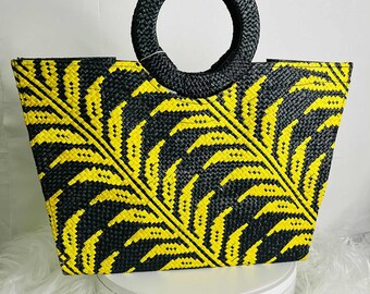 May include: A black and yellow woven tote bag with a leaf pattern. The bag has a circular black handle and is made of a textured material. The bag is approximately 12 inches wide and 10 inches tall.