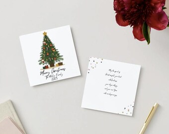 May include: Two white square Christmas cards. One card features a decorated Christmas tree with the text "Merry Christmas" and the family name. The second card has a message with gold and silver confetti accents. A gold pen and a burgundy flower are also visible.