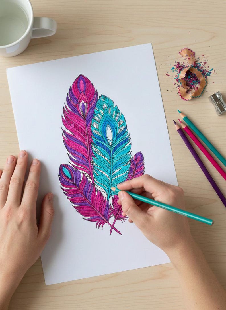 A lifestyle preview of a person's hands coloring a detailed feather illustration featuring vibrant teal, magenta, and purple patterns. This 60-page collection showcases high-quality bohemian line art set on a light wooden desk with art supplies, perfect for adult relaxation, mindful meditation, and printable Zen activities.