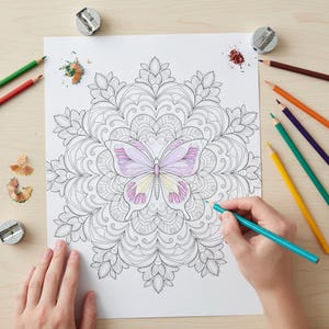 May include: A person coloring a detailed butterfly design on a white paper with colored pencils. The butterfly is colored in shades of pink and yellow. Pencil sharpeners and pencil shavings are scattered around the paper on a light wood surface.