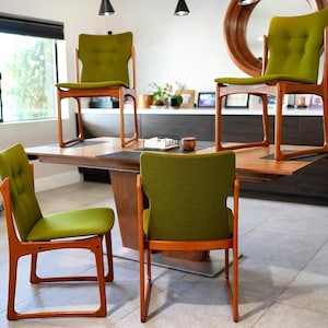 May include: Four dining chairs with light brown wooden frames and olive green upholstered seats and backrests. Each backrest features two tufted buttons. Two chairs are positioned on the floor, while two are placed on a wooden dining table.