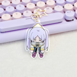 May include: A clear acrylic keyring featuring a cartoon character with long light purple hair in twin tails, pointed ears, and a white and gold outfit. The character has a sad expression and is attached to a gold-coloured star-shaped metal clasp.