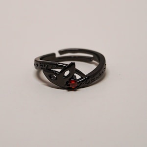 K&ouml;nnte beinhalten: Verstellbarer schwarzer Ring mit einem Fuchskopf-Design und einem kleinen roten Edelstein. Der Ring hat ge&auml;tzte Details und ist vor einem wei&szlig;en Hintergrund platziert. Ein einzigartiges Schmuckst&uuml;ck.