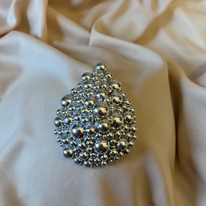 May include: A silver teardrop-shaped brooch made of many small, round beads.