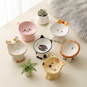 Puede incluir: Colección de cuencos de cerámica para mascotas con formas de animales, incluyendo un cerdo, un conejo, un gato, un ciervo, un león y un tigre. Cada cuenco presenta un diseño y esquema de color únicos.