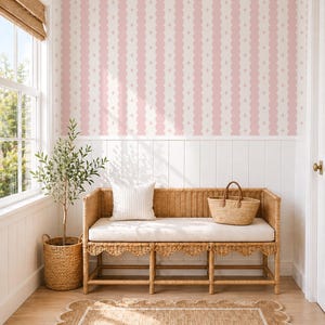 May include: A light-filled room with a woven bench, a striped pillow, and a woven basket. The room features a jute rug with a scalloped edge and a pink and white patterned wallpaper. A small potted tree sits in a woven basket.