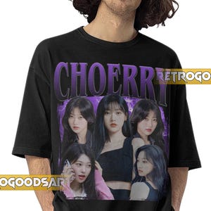 May include: Black t-shirt featuring a purple graphic with the word "CHOERR" and a group of women. The shirt has a vintage aesthetic with the text "RETROGOOD" and "RETROGOODSART" in the corners.