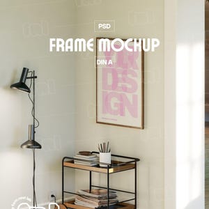 Könnte beinhalten: Innenraum mit einem gerahmten Poster mit rosa Text "DESIGN". Eine schwarze Stehlampe und ein Rollwagen mit Büchern und einer weißen Tasse sind ebenfalls zu sehen. Der Text "FRAME MOCKUP" wird angezeigt. Der Rahmen ist DIN A.