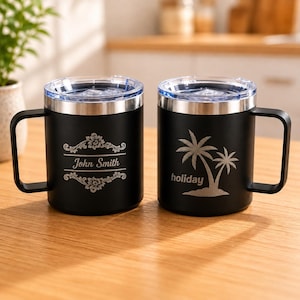 May include: Two black stainless steel mugs with clear lids and handles. The left mug features an engraved floral frame with the text John Smith. The right mug displays an engraved palm tree graphic above the word holiday in lowercase letters.