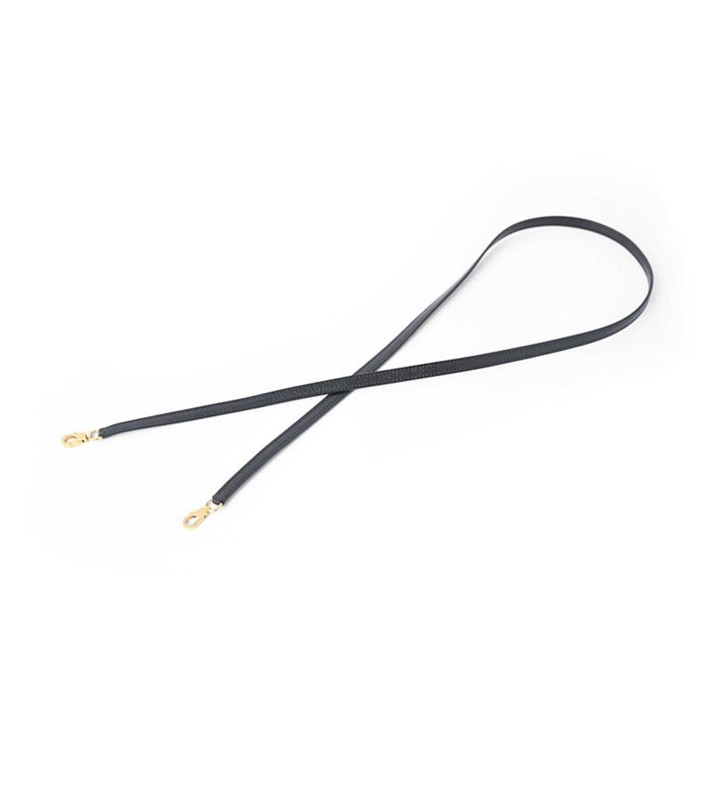 May include: A black, thin strap with gold-colored clasps on each end. The strap is designed to be used as a replacement or accessory for a handbag or purse. The strap is shown against a white background.