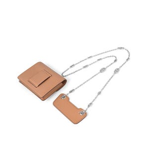 May include: A tan leather crossbody bag and phone holder set with a silver chain strap. The bag is rectangular with a flap closure. The phone holder is also tan leather and rectangular with a silver chain attachment.