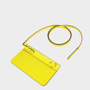 May include: A bright yellow crossbody bag with a long, thin strap. The bag is rectangular with a flap closure and a textured surface. The strap is yellow on the outside and brown on the inside.