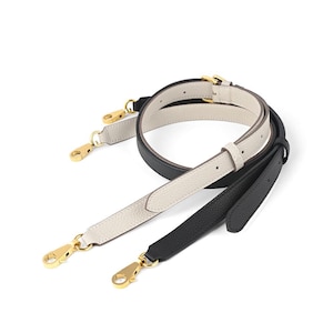 May include: Three leather purse straps in black, cream, and black. Each strap has gold-colored metal clasps and adjustable buckles. The straps are designed for handbags and purses.