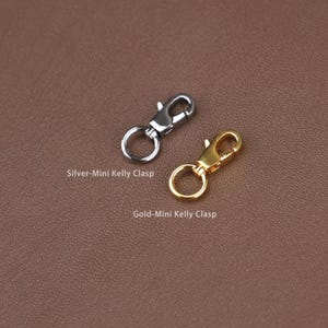 May include: Two mini Kelly clasps, one silver and one gold, are displayed against a brown background. The silver clasp is labeled "Silver-Mini Kelly Clasp" and the gold clasp is labeled "Gold-Mini Kelly Clasp".