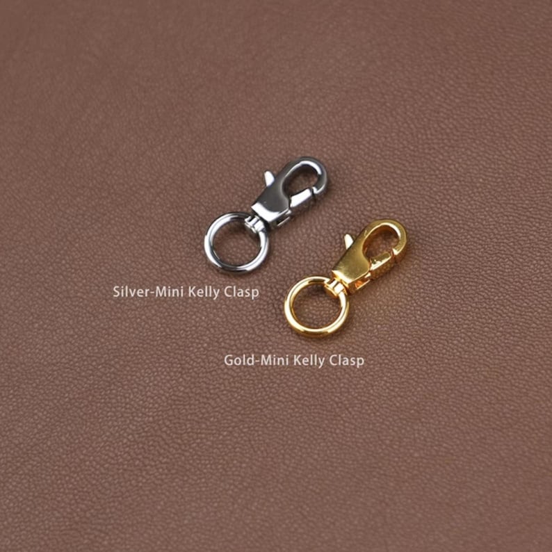 May include: Two mini Kelly clasps, one silver and one gold, are displayed against a brown background. The silver clasp is labeled "Silver-Mini Kelly Clasp" and the gold clasp is labeled "Gold-Mini Kelly Clasp".