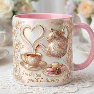 May include: A ceramic mug with a pink handle and interior, featuring a teapot and teacup design with gold accents. The mug has the text "I'm the tea you'll be having" and is decorated with floral patterns.