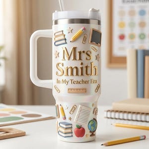 May include: A white iridescent tumbler with a handle and straw featuring gold text that reads Mrs Smith In My Teacher Era. The surface is decorated with 3D-style icons including stacks of books, pencils, paperclips, a chalkboard, a ruler, and a globe.