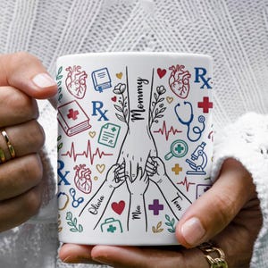 Puede incluir: Taza de cerámica blanca con ilustraciones médicas y la palabra "Mommy", además de los nombres Olivia, Mia y Tom. La taza incluye corazones, un estetoscopio y una cruz médica.