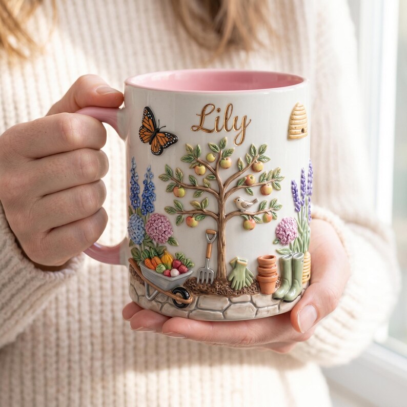 May include: A white ceramic mug with a pink interior and handle, featuring a garden-themed relief design. The design includes a tree with apples, a butterfly, a wheelbarrow, and the name "Lily". The mug has a textured, detailed appearance.