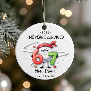 Op de afbeelding: Een witte keramische kerstbal met een gouden touwtje. De bal toont de tekst "-2025- THE YEAR I SURVIVED" en een cartoonwolk met de cijfers 6 en 7. De tekst "Mrs. Diana FIRST GRADE" is ook aanwezig.