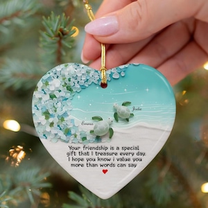 May include: Heart-shaped ornament with a beach scene featuring two sea turtles and the names "Emma" and "Jodie." The ornament has a gold string for hanging and includes the text: "Your friendship is a special gift that I treasure every day. I hope you know I value you more than words can say."
