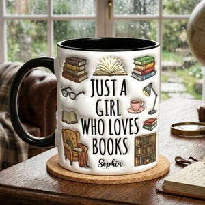 Pu&ograve; includere: Tazza in ceramica bianca con manico e bordo neri, decorata con illustrazioni a tema libri e la scritta "JUST A GIRL WHO LOVES BOOKS" e il nome "Sophia". La tazza &egrave; appoggiata su un sottobicchiere rotondo in sughero.