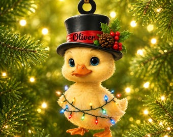 May include: A yellow duckling Christmas ornament wearing a black top hat with a red band featuring the name Oliver in black script. The hat is decorated with holly leaves, red berries, and a pinecone. The duckling is wrapped in colorful string lights.